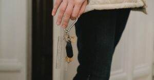 A close-up photo of an adult hand holding a set of house keys indoors, suggesting security and home access.