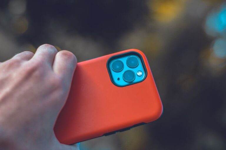Pixel 11 en 2026 : les écarts entre les modèles A close-up view of a hand holding a smartphone with an orange case and three camera lenses.