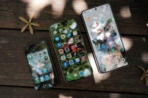 A collection of smartphones showing different app icons, placed on a wooden surface in natural light.