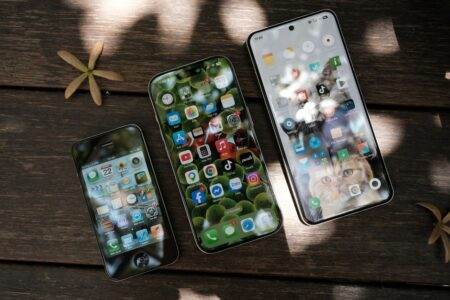 A collection of smartphones showing different app icons, placed on a wooden surface in natural light.