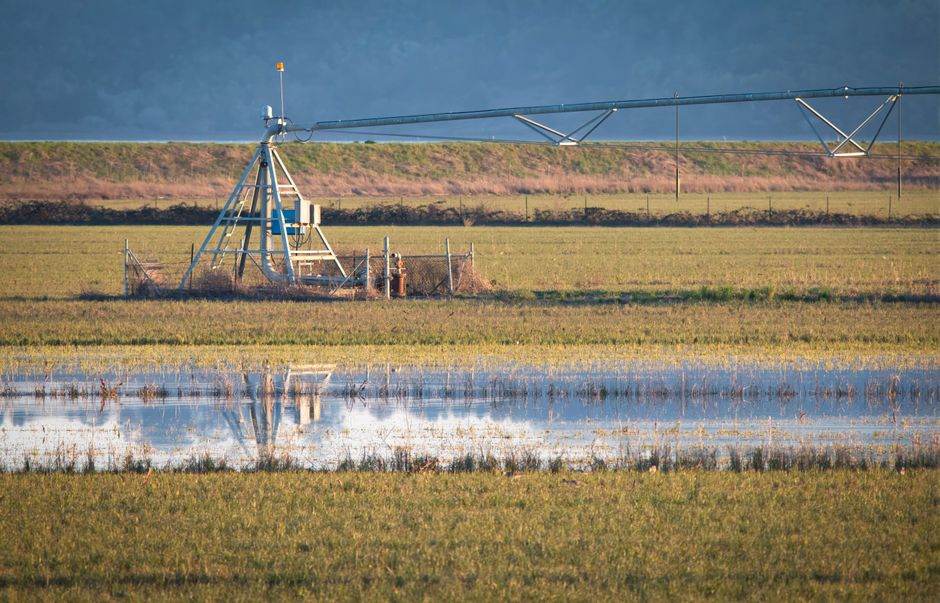 A flooded farm field with an irrigation system and reflection under cloudy skies.