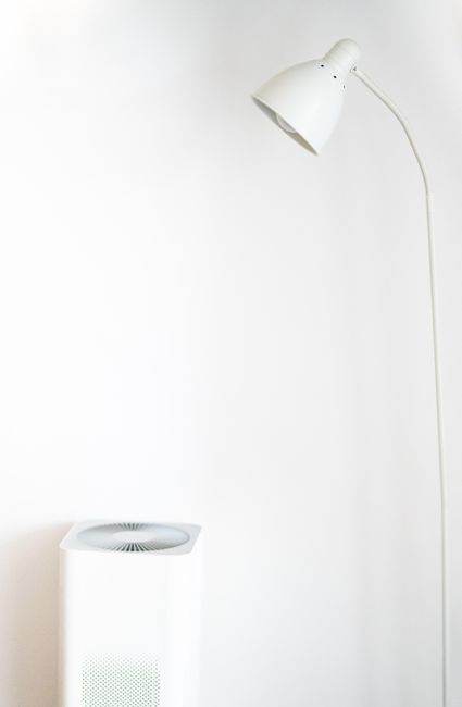 A minimalist room featuring a white floor lamp and air purifier against a blank wall.