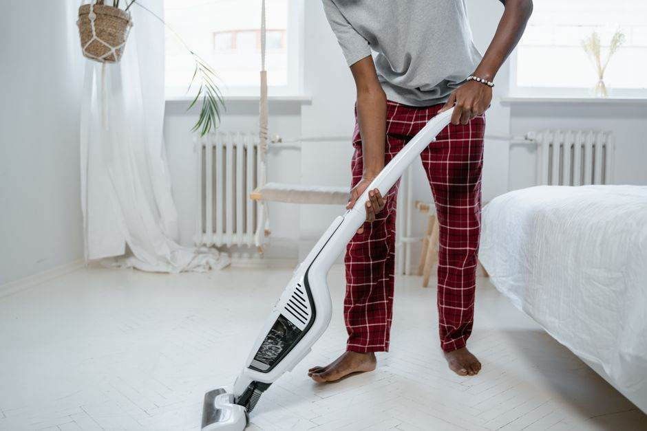 A person cleaning a bedroom with a modern vacuum cleaner, showcasing casual home lifestyle.