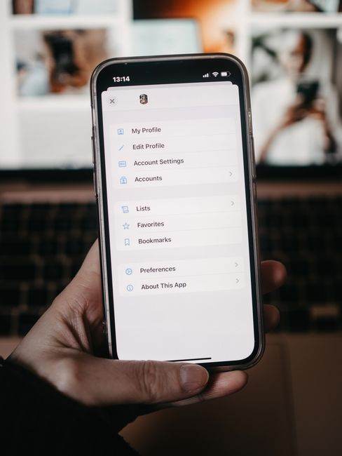 A person holds a smartphone showing the settings menu in front of a blurred background.