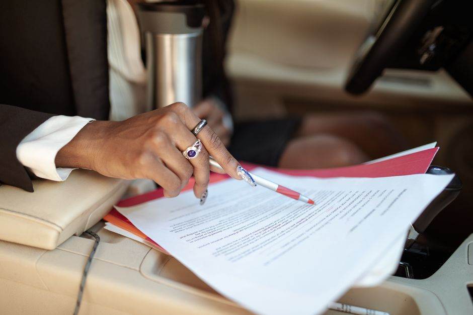 A professional reviewing documents in a car interior, focusing on hand and paperwork.
