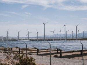A renewable energy farm with wind turbines and solar panels under a clear sky.