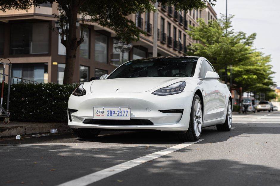 A sleek white Tesla Model 3 parked on a city street under trees, showcasing modern automotive design.