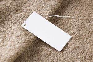 Close-up of a blank white price tag on textured beige fabric, ideal for branding use.