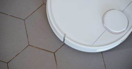 Droit à la réparation européen en 2026 : smartphones, lave-linge, aspirateurs, qui est concerné? Close-up of a robotic vacuum cleaner on hexagonal tiles for efficient cleaning.