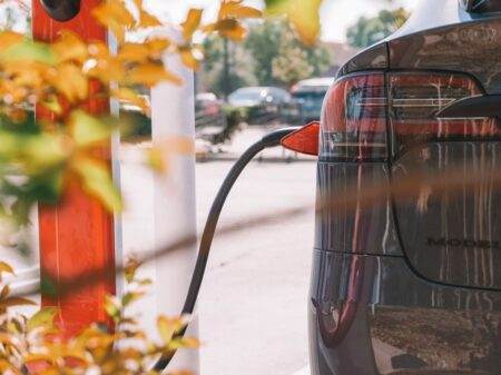 Voiture électrique d’occasion en 2026 : le budget passe sous celui d’une vieille voiture thermique Close-up of an electric car charging at a station with blurred cars in the background.