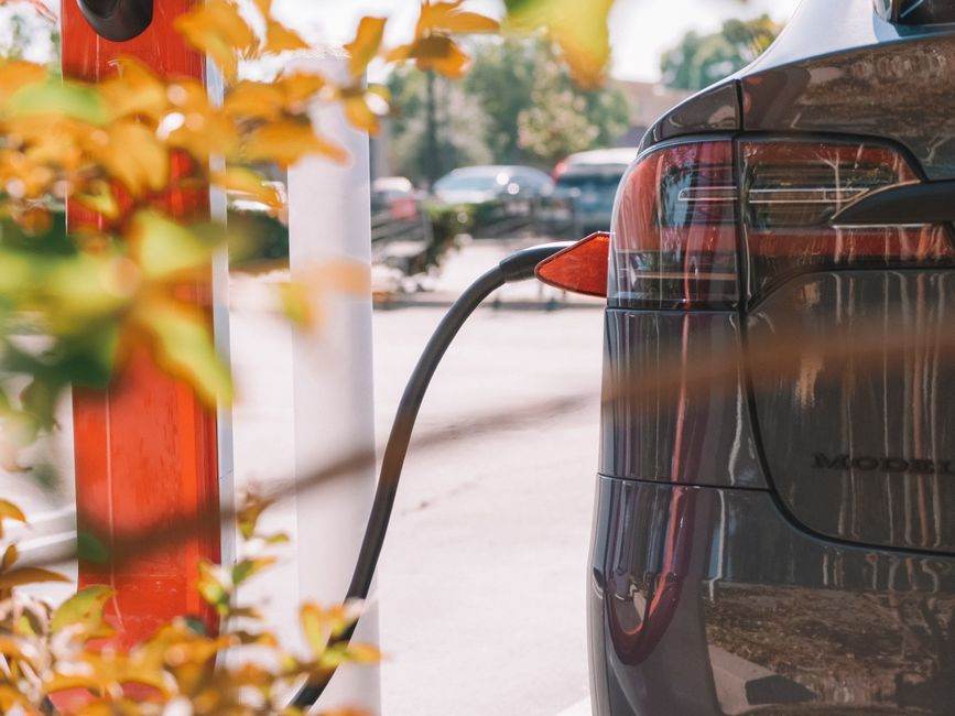Voiture électrique d’occasion en 2026 : le budget passe sous celui d’une vieille voiture thermique Close-up of an electric car charging at a station with blurred cars in the background.