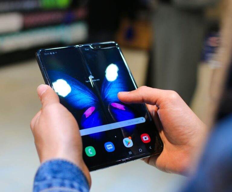 Galaxy Z Fold 8 Ultra face au Honor Magic V6 : deux compromis Close-up of hands holding a foldable smartphone showing a butterfly on the screen.