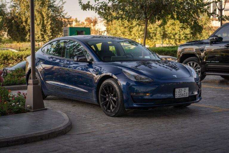 Tesla Model 3 : les pneus font gagner 38 km au WLTP Electric blue Tesla Model 3 parked in sunlit commercial parking area.