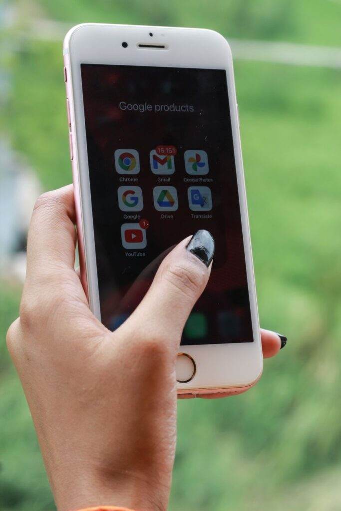 Hand with black nails holding a smartphone showing Google apps outdoors.