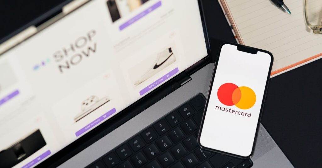 Compte SumUp en 2026 : cashback plafonné, retraits limités et pas d’IBAN français Laptop and smartphone with Mastercard logo, illustrating online shopping and digital payments.