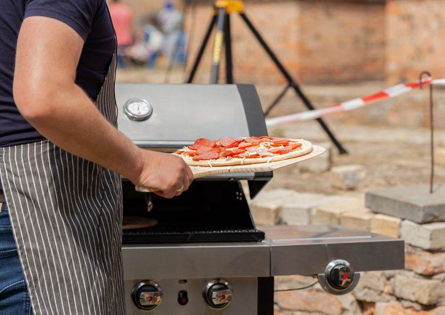 Man grilling a homemade pizza with pepperoni on an outdoor barbecue grill.