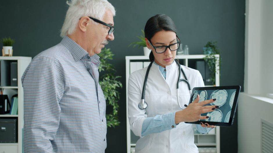 IA en santé en 2026 : le contrôle a un prix Medical professional reviewing brain scans with an elderly man in a clinic.