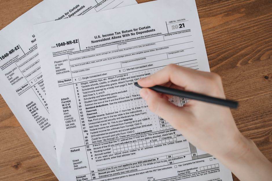 Person filling out U.S. tax form 1040-NR-EZ with a pen on a wooden table.