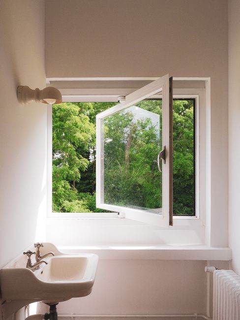 Simple white bathroom with a view of greenery through an open window.