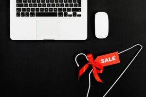 Stylish flat lay of a laptop, mouse, and sale tag on a hanger for online shopping concept.