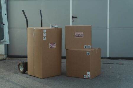 Logistique export en France : quelles entreprises comparer en 2026? Three cardboard boxes on a dolly, ready for shipping outside a warehouse.