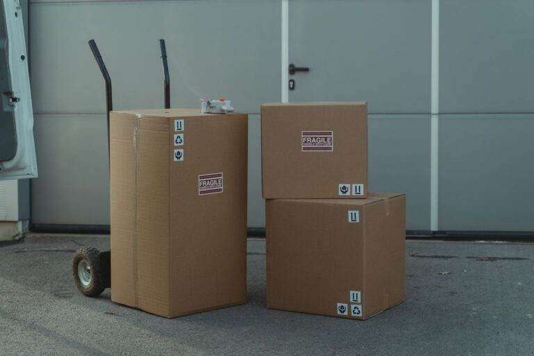 Logistique export en France : quelles entreprises comparer en 2026? Three cardboard boxes on a dolly, ready for shipping outside a warehouse.
