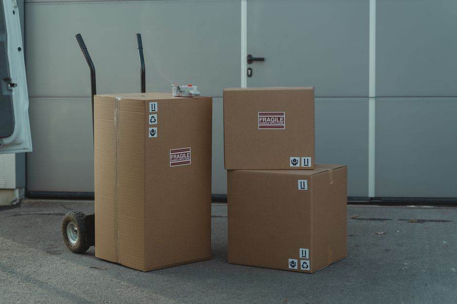 Logistique export en France : quelles entreprises comparer en 2026? Three cardboard boxes on a dolly, ready for shipping outside a warehouse.