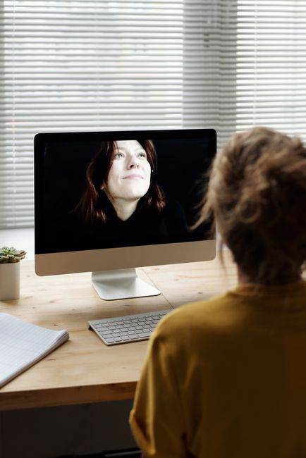 Woman using desktop computer for video call from home office.