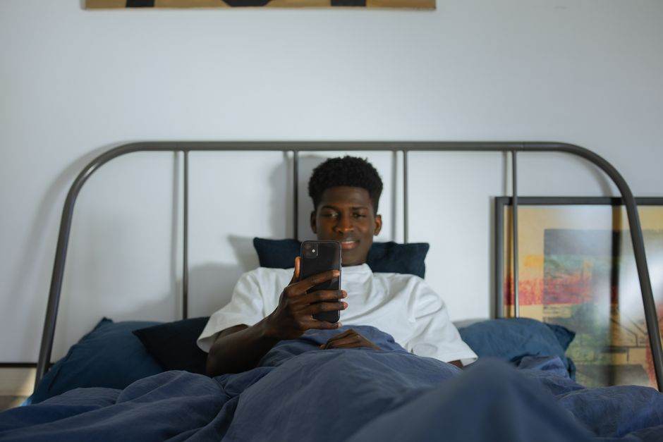 Young man using smartphone in bed, enjoying leisure time at home.