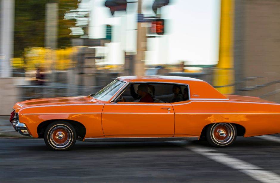 A classic orange car driving quickly through city streets, capturing motion and nostalgia.