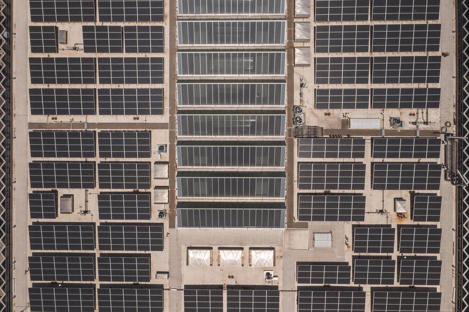 A high-angle drone shot capturing a grid of solar panels on a large industrial rooftop, showcasing renewable energy.