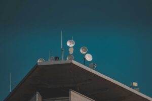 A low-angle view of communication dishes and antennas on a building against a clear blue sky.