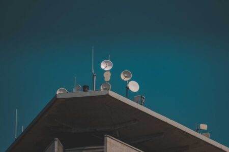 Communications par satellite en 2026 : 5G, antennes et sécurité A low-angle view of communication dishes and antennas on a building against a clear blue sky.