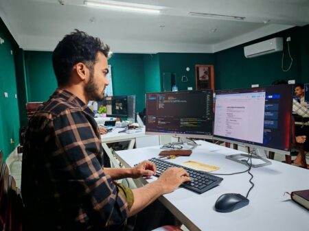 Claude Sonnet 5.5 : vitesse, prix et coût par tâche A software developer working on code at a dual monitor setup in a modern office.