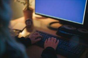 A woman typing on a keyboard in a dimly lit, cozy workspace, featuring a computer screen.