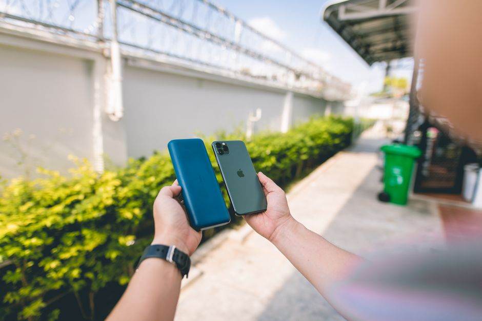 Recharge rapide : les watts ne suffisent pas Close-up of a smartphone and power bank held in hands in an outdoor setting.