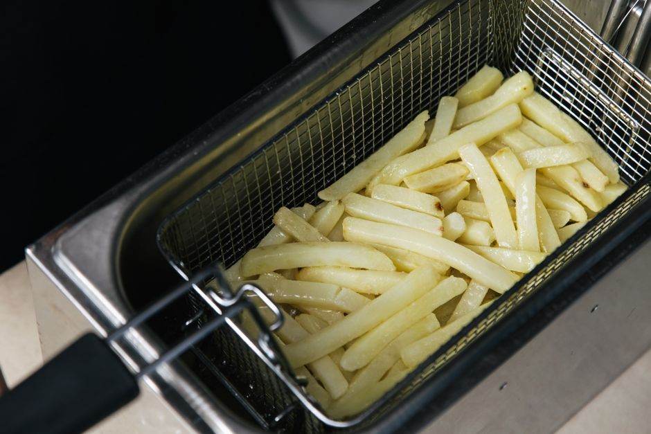 Air fryer sans PFAS : le revêtement ne règle pas tout en 2026 Close-up of raw french fries in a deep fryer basket ready for cooking.