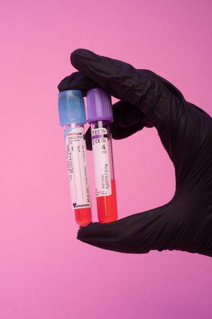 Crop anonymous medical specialist in black latex gloves demonstrating test tubes with blood samples against pink background