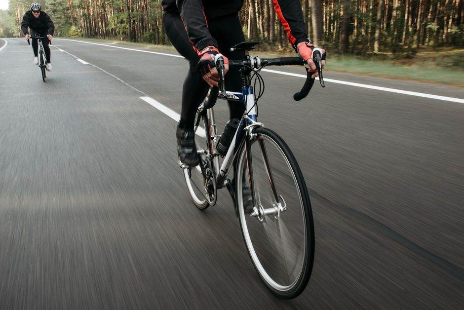 Cyclists racing on an open road surrounded by nature, showcasing speed.