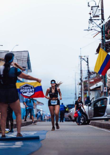 Female runner in a Colombian street marathon, showcasing athletic strength and cultural pride with flags.