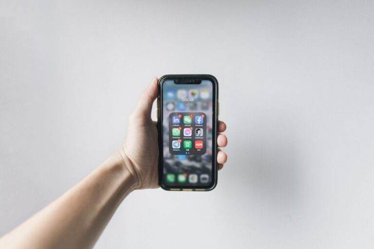 Hand holding smartphone displaying social media apps on home screen.