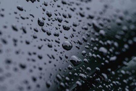 High-definition close-up of raindrops on a reflective surface with a dark background.
