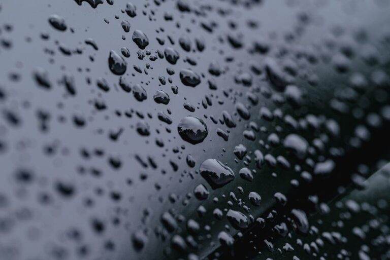 High-definition close-up of raindrops on a reflective surface with a dark background.