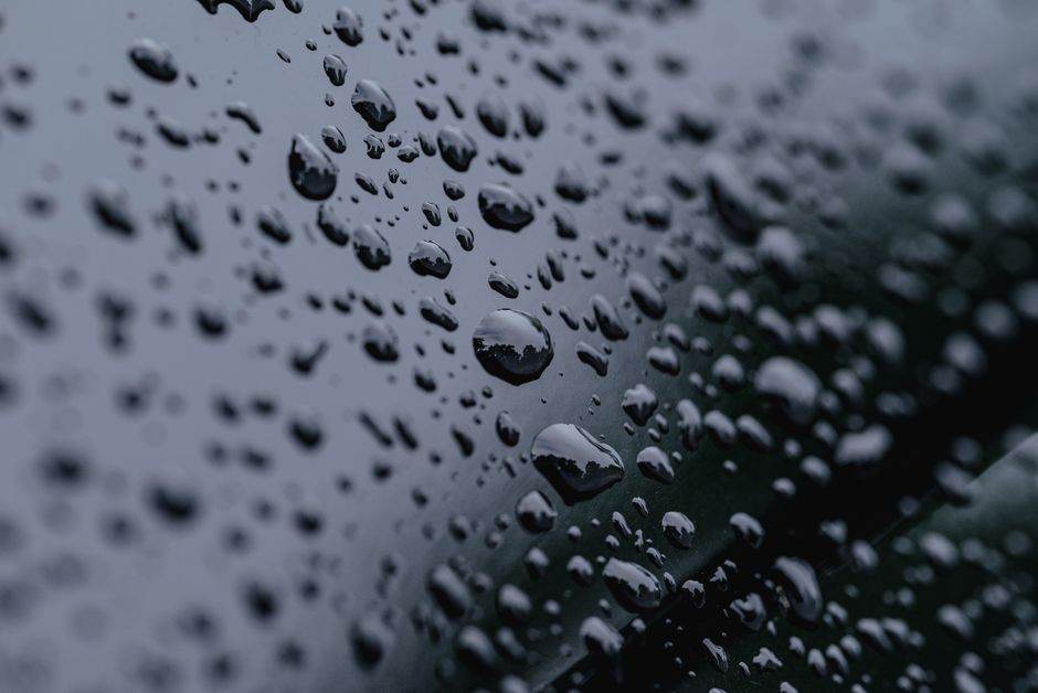 Énergie de la pluie en 2026 : des volts, peu de watts High-definition close-up of raindrops on a reflective surface with a dark background.