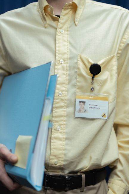 Man in yellow shirt holding documents with visible ID badge in office setting.