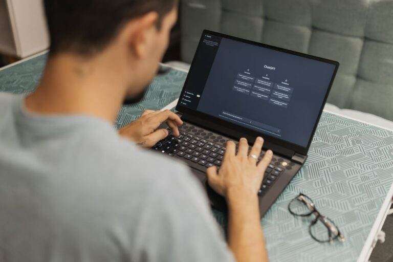 Man using laptop with AI interface, typing with focused attention. Indoors with eyewear beside.