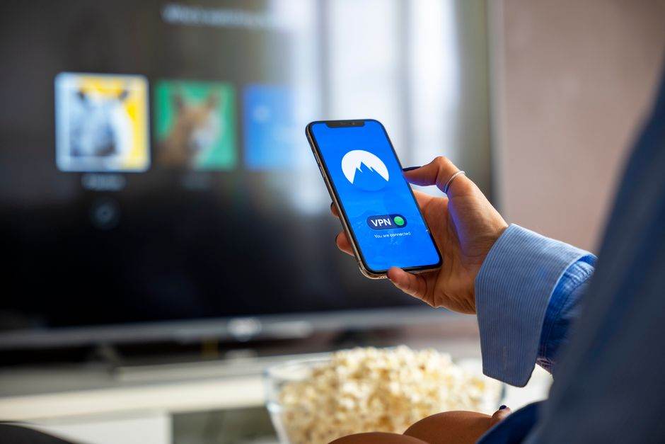 Streaming gratuit en 2026 : replay, publicité et pièges Person using VPN on smartphone while watching smart TV at home.