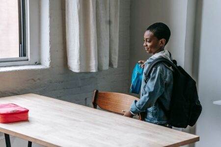 Mal de dos à l’école en 2026 : cartable, posture, exercices Side view of cute African American child holding lunch box while preparing for snack in school