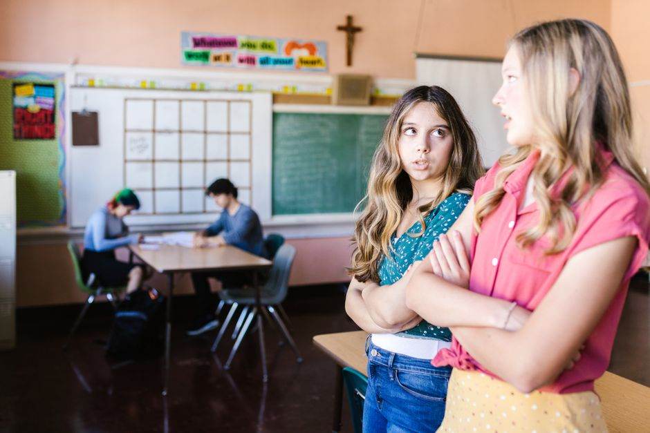 Teenage girls having a conversation in a school classroom setting.
