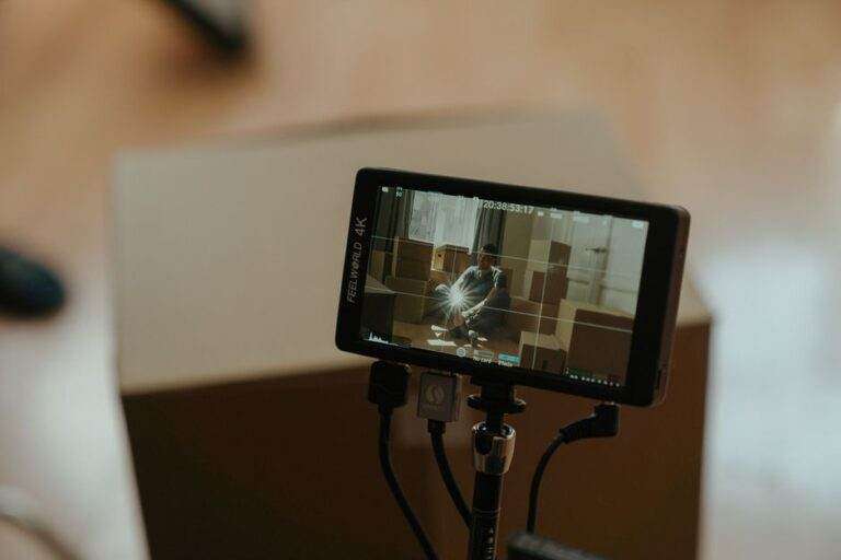 Mode Filmmaker sur TV en 2026 : réglages et limites A camera monitor shows a scene with a person sitting among boxes, highlighting the filming process.